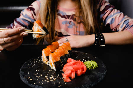 modern sushi rolls with ginger and wasabi. Traditional japanese meal. Healthy nutrition. Woman holding a roll with chopsticksの写真素材