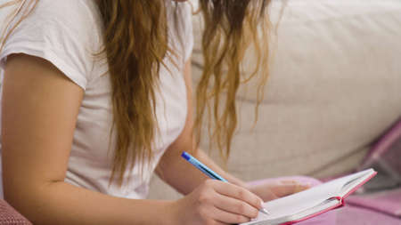 relaxed studying style. home education. casual teenage girl sitting on a sofa writing in her notebookの写真素材