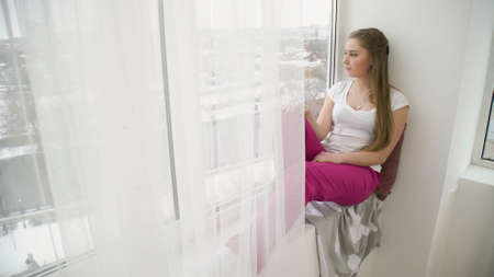 relaxing leisure. young pensive thoughtful teen girl sitting on the windowsill and looking out of the windowの写真素材