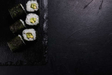 sushi rolls with salmon covered in nori on dark background. Japanese traditional food preparing craft. Copy space conceptの写真素材