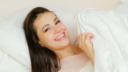 happy leisure. comfortable bedding. flirty playful smiling young beautiful sexy girl laying on the...