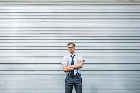 serious confident purposeful motivated ambitious young stylish hipster business man with crossed arms, standing against grey wall background outdoor. copy space conceptの写真素材