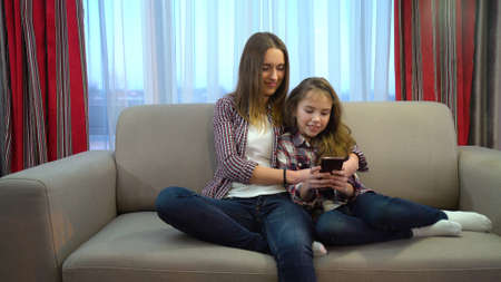 idleness lazy family leisure. modern lifestyle problems. internet and social network addiction. mom and little girl browsing smartphone at home on the couchの写真素材