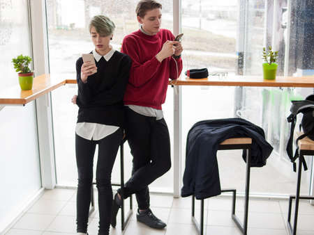 youth lifestyle. mobile phone addiction. internet communication. young man and girl standing in a cafe or bar looking at their smartphones texting or chatting onlineの写真素材