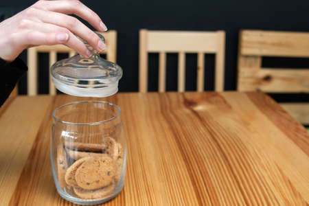 pastry food. tasty chocolate chip cookies. woman hand removing jar lid to taste some buscuits