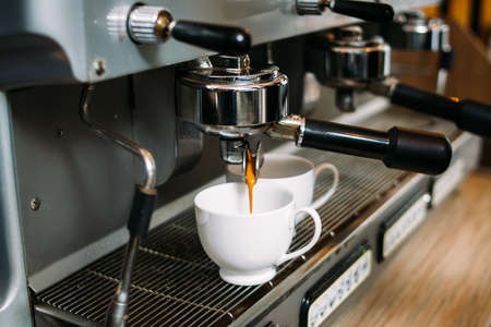 drink pouring from coffee making machine into two white cups. morning caffeine intake ritual. tasty hot dose of energyの写真素材