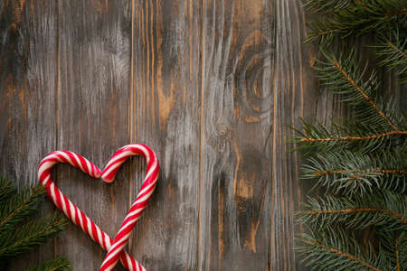 festive minimalistic holiday decor background. seasonal design with fir tree branch and candy cane in heart shape on grey wooden backdrop with free space.の写真素材