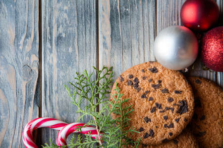 festive christmas decor. balls candy cane chocolate chip cookies and juniper twig on rustic wooden background.の写真素材