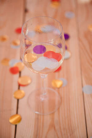 Party over concept. Half empty glass with wine and confetti on wooden background.の写真素材