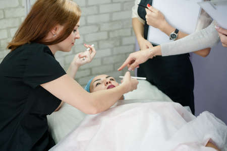 Professional cosmetology courses. Permanent makeup. Female beautician teaching how to outline eyebrows.の写真素材