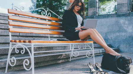 Workaholic lifestyle. Modern technology. Busy woman sitting on bench working on laptop.