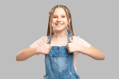 Happy child portrait. Like gesture. Cheerful girl showing thumbs up smiling isolated on neutral background.の写真素材