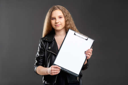 Youth career. Startup project. Ambitious teen girl showing blank paper for contract on clipboard isolated dark.の写真素材