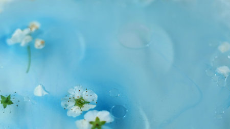 Floral serum. Essential oil. Defocused blue white color gel bubble texture fluid cherry blossom flower petal floating in water abstract art background.の写真素材
