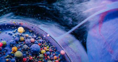 Multicolor fluid. Bubble paint. Layered oil spot drop violet yellow purple foam ink floating on...