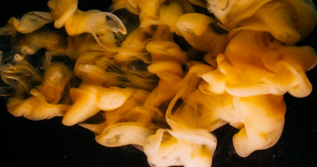 Paint vapor. Liquid pigment. Blur yellow color water smoke wave swirling acrylic particles floating on abstract dark black background.の写真素材
