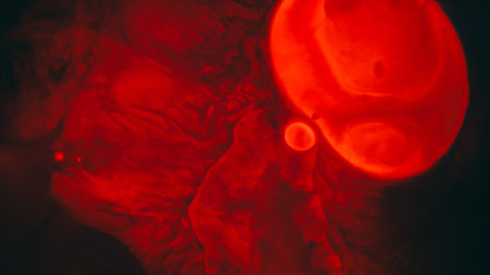 Liquid spot. Stains oil background. Defocused red neon color water splatter paint round flow fluid on abstract dark black texture.の写真素材