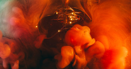 Ink steam. Dye swirl. Red orange smoke mix color in glowing garland liquid. Sparkling bokeh light...