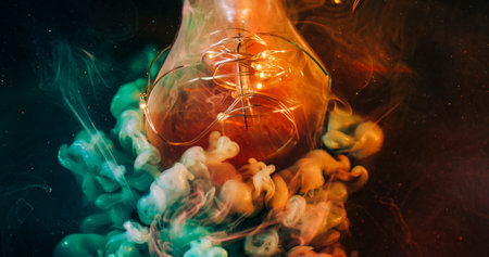 Defocused sparkling flow. Light bulb night. Shimmering green orange blob paint. Color particles swirl on garland black abstract background.の写真素材