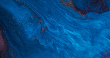 Spilling fluid. Mix color. Defocused blue orange bronze shimmer ink texture spreading splash floating on abstract acrylic background.の写真素材