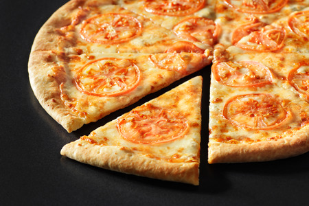 Cut Pizza close up margarita on black stone background with Tomatoes, Cheese Mozzarellaの写真素材