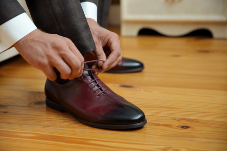 closed lacing, a man laces up his shoes on a wooden floorの写真素材