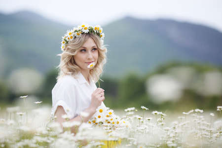 pretty young blonde woman with camomiles in white blooming field. girl in camomile wreathの写真素材