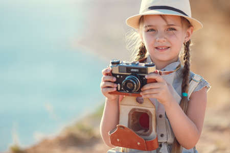 child girl traveler. trip alone. girl walking with camera and suitcase on nature by sea. travel,...
