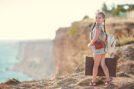 child girl traveler. trip alone. girl walking with camera and suitcase on nature by sea. travel, vacation, holidaysの写真素材
