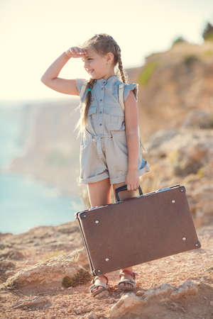 child girl traveler. trip alone. girl walking with camera and suitcase on nature by sea. travel,...