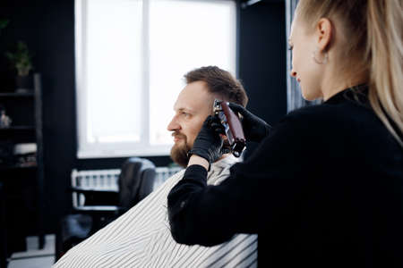Portrait of a man in Barbershop, shave and cut by barber girl