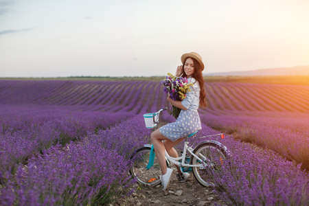 pretty brunette woman running away in lavender field. woman in dress and straw hat having fun in flowers of lavenderの写真素材
