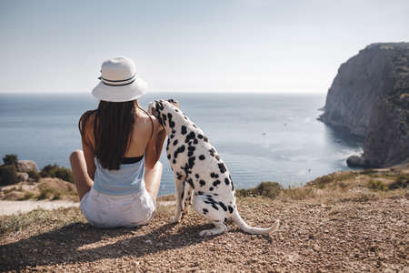 Woman with a dog dalmatian. back sit girl and her friend dog on the blue sea backgroundの写真素材