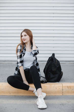 Young fashion woman sitting outdoors near gray backgroundの写真素材
