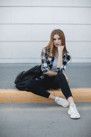 Young fashion woman sitting outdoors near gray backgroundの写真素材