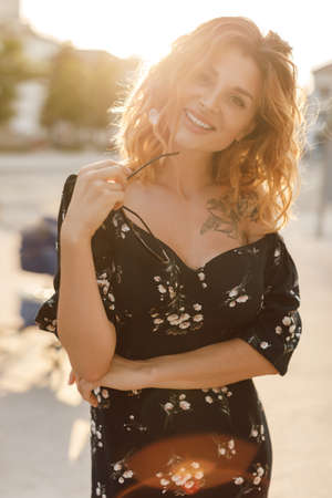 happy young woman walking on city street in sunset warm light. Smiling emotional girl outdoors in...