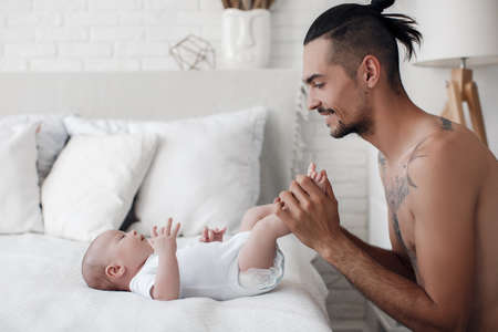 man with infant. happy family at home. happy father with cute two months baby boy laying in light bed at homeの写真素材