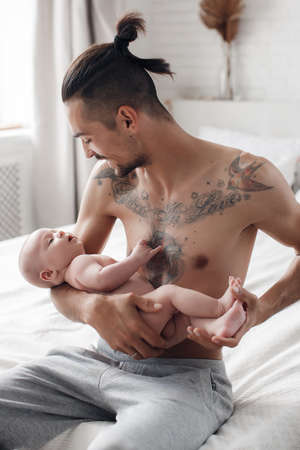 man with infant. happy family at home. happy father with cute two months baby boy laying in light bed at homeの写真素材