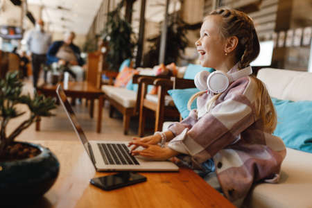 cute little girl using laptop in terrace cafe
