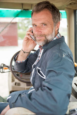 Farmer leaning on the tractor using a smartphone