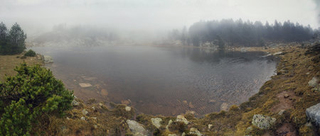 Mystical fog rising over a mountain forest, with serene reflections in the lakeの写真素材