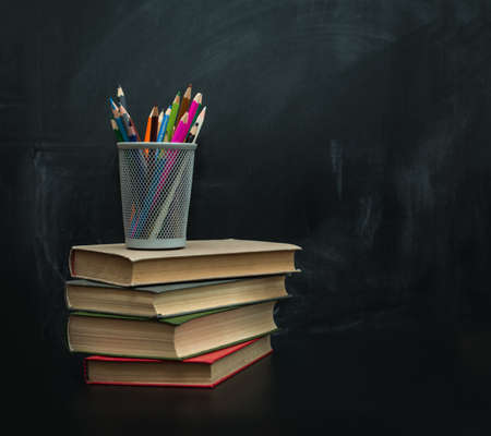 stack of books, cup of crayons and red apple against the black school board for chalk drawingのeditorial素材