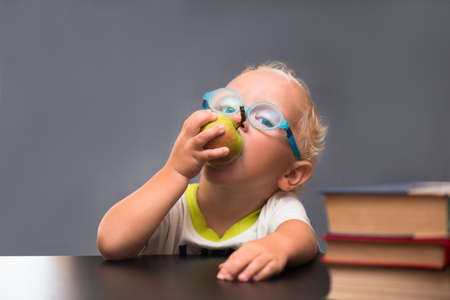 Child with glasses sits at a table and eating an appleの写真素材