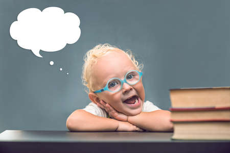 Child with glasses sits at a table and above it a cloud of thoughtsの写真素材