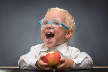 The child wears a white shirt sits at a table and eating an appleの写真素材