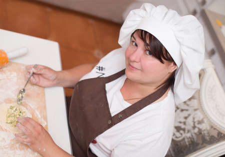 A girl wearing a kitchen apron and chef hat cooking cakesの写真素材