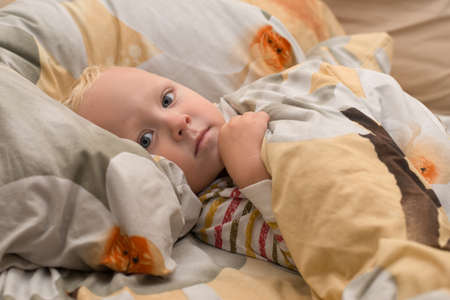 Sad sick baby lying on the bedの写真素材