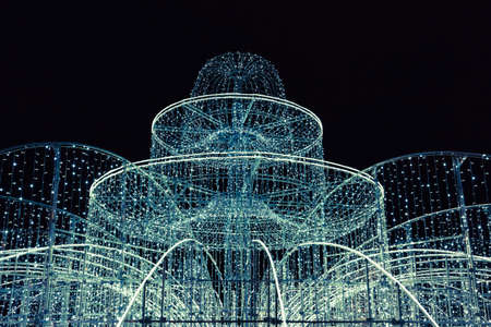 Illuminated fountain decorated with garlands, festive illuminations and christmas lights, decoration elements at night. Streets of the city decorate for the New Year. Winter holiday concept.の写真素材