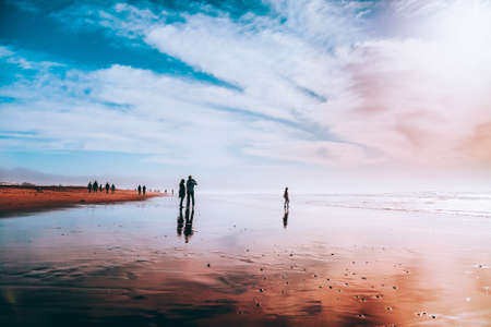 Silhouettes of people enjoying on the beach. Wet sand and low tide.の写真素材