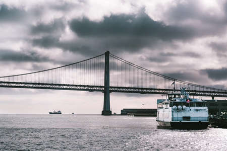 Suspension Oakland Bay Bridge in San Francisco, California, USA. Tourist ferry boat anchoring in port. Landscape in storm. Black and white monochrome view.の写真素材